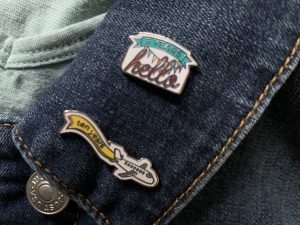 2 small enamel pins on a denim jacket collar
