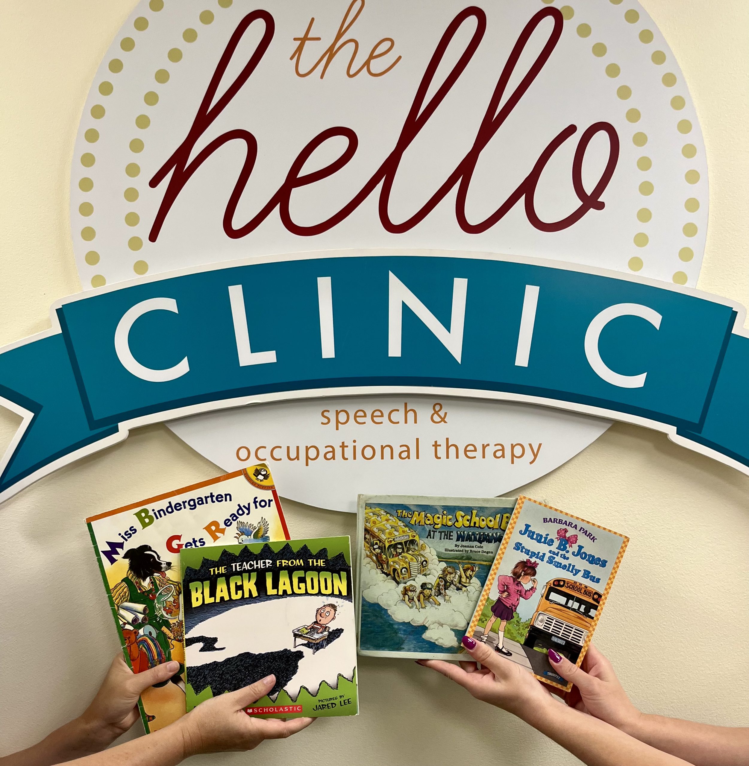 Two pairs of hands holding up four picture books in front of The Hello Clinic sign.